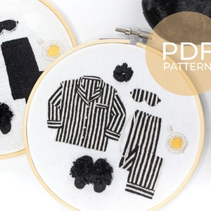 May include: Two embroidery hoops with white fabric and black embroidery designs. The designs include a pair of pajamas, slippers, an eye mask, and a cup of coffee. The text "PDF PATTERN" is visible in the top right corner of the image.