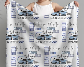 May include: A white baby blanket with a blue and gray racing car pattern. The blanket features the name "Ethan Mello" repeated throughout the design.