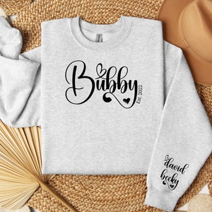 May include: A gray sweatshirt with the text "Bubbly Est. 2022" in black cursive lettering. The sweatshirt has a black heart design on the left sleeve with the text "david becky" in black cursive lettering.