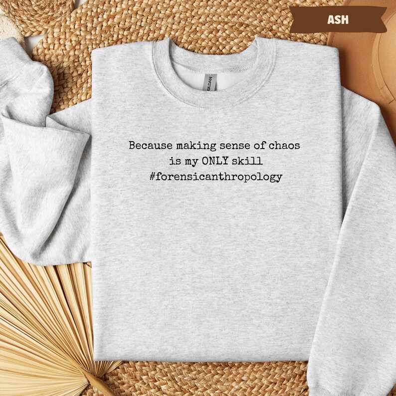 May include: Ash-colored sweatshirt with the text "Because making sense of chaos is my ONLY skill #forensicanthropology" in black. The sweatshirt is a crew neck style and is made of a soft material.