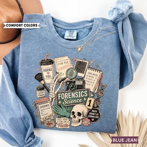 May include: Blue jean colored sweatshirt with a graphic design featuring forensic science elements. The design includes a skull, magnifying glass, camera, and the words "Forensics Science". The sweatshirt also has the text "Evidence Fuel" and "Truth Doesn't Lie Evidence Does".