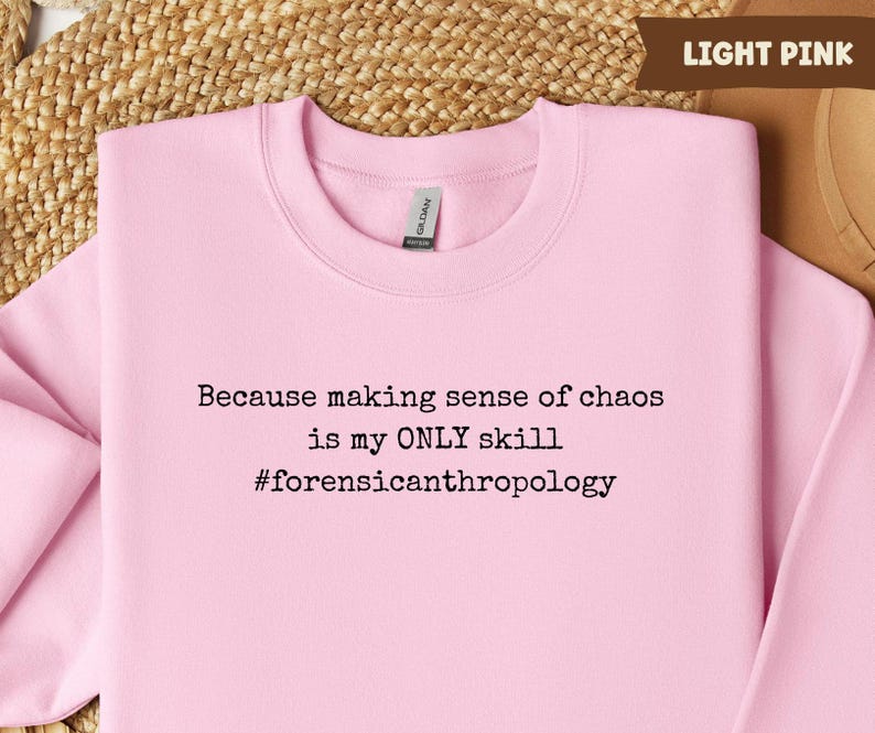 May include: Light pink sweatshirt with the text "Because making sense of chaos is my ONLY skill #forensicanthropology" in black. The sweatshirt is a crew neck style.