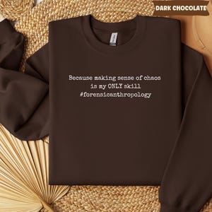 May include: Dark chocolate-colored sweatshirt with the text "Because making sense of chaos is my ONLY skill #forensicanthropology" in white. The sweatshirt is a crew neck style and has long sleeves.
