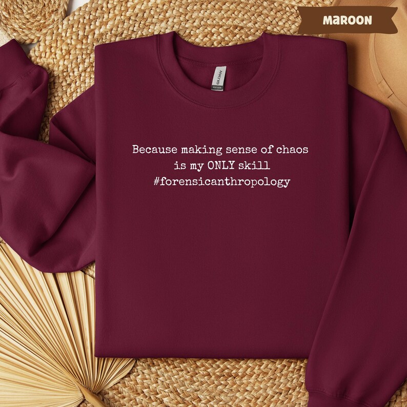 May include: Maroon crewneck sweatshirt with white text that reads "Because making sense of chaos is my ONLY skill #forensicanthropology". The sweatshirt is made of a soft material and is a solid maroon color.