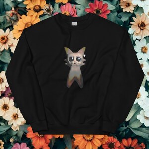 Puede incluir: Sudadera negra con un diseño de gato de dibujos animados. El gato tiene ojos grandes y un cuerpo gris claro con un degradado de colores. La sudadera está hecha de un material suave, adecuada para uso casual.