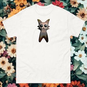 May include: White t-shirt with a graphic of a cartoon cat with large eyes and a wide smile. The cat is peeking out of a hole in the shirt.