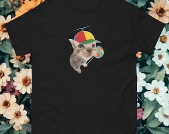 May include: Black t-shirt featuring a graphic of a cat wearing a colorful propeller hat and holding a rainbow lollipop. The cat is light gray with darker stripes. The hat is red, yellow, and green. The lollipop has a swirl design.