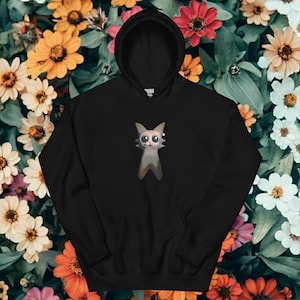 Puede incluir: Sudadera con capucha negra con un diseño de gato de dibujos animados. El gato tiene ojos grandes y un cuerpo gris con un degradado de colores. La sudadera tiene un bolsillo delantero y una capucha con cordón.