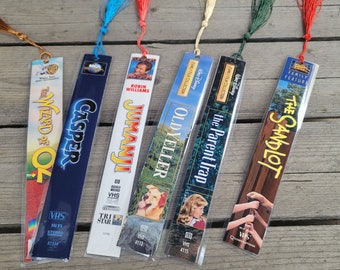 May include: Six colorful bookmarks with movie titles and VHS tape designs. The bookmarks feature titles like "The Wizard of Oz", "Casper", "Jumanji", "Old Yeller", "The Parent Trap", and "The Sandlot".