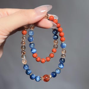 May include: Two beaded bracelets, one with blue and brown beads and the other with orange beads. The bracelets are stacked on top of each other.