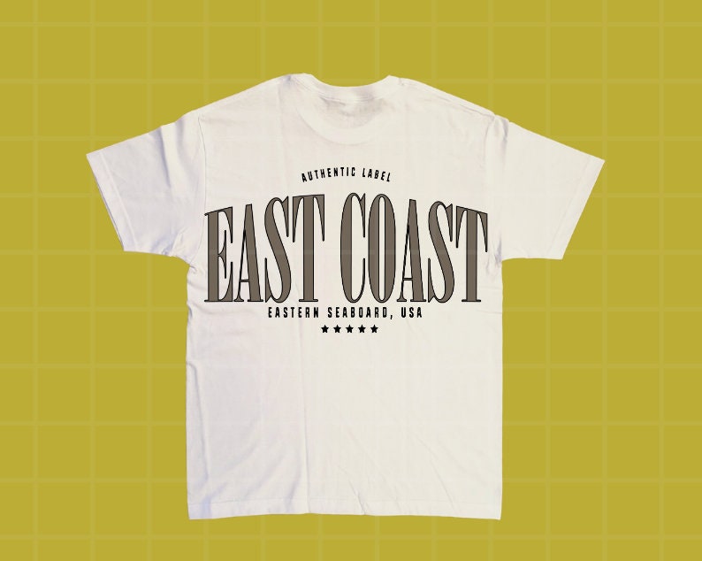 Może przedstawiać: Biała koszulka z napisem "EAST COAST" dużymi, ciemnoszarymi literami. Nad tekstem znajduje się "AUTHENTIC LABEL", a pod nim "EASTERN SEABOARD, USA" z pięcioma gwiazdkami. Koszulka wykonana jest z miękkiego materiału.