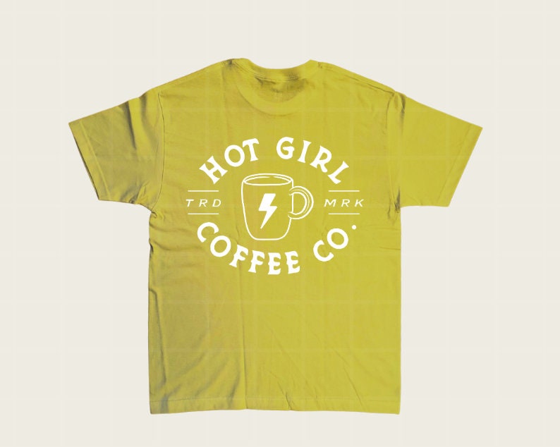 Puede incluir: Una camiseta verde amarillenta con un gr&aacute;fico blanco. El gr&aacute;fico presenta una taza de caf&eacute; con un rayo en el interior y las palabras "HOT GIRL COFFEE CO." en un dise&ntilde;o circular. La camiseta tiene cuello redondo y mangas cortas.