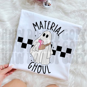 May include: White t-shirt with a black and white chequered pattern, a ghost holding a pink drink, and the text "Material Ghoul".
