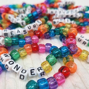 May include: A close-up of colorful beaded bracelets with letter beads spelling out words like "treasure", "wonder", "pixie", and "ur".