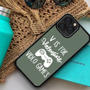 May include: A green and black phone case with a white graphic of a video game controller and the text "V is for Video Games".