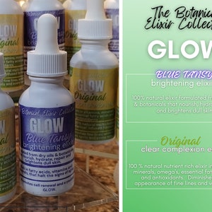 Pu&ograve; includere: La collezione di elisir botanici: Due flaconi di vetro di siero per il viso, uno etichettato "Glow Original Clear Complexion Elixir" e l'altro etichettato "Glow Blue Tansy Brightening Elixir". Entrambe le bottiglie hanno tappi contagocce bianchi e sono su una superficie trasparente.