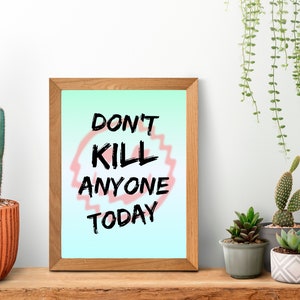 Puede incluir: Una impresión enmarcada con un fondo degradado azul claro y verde. La impresión presenta el texto "Don't Kill Anyone Today" en letras negras con un círculo rosa alrededor de la palabra "Kill". La impresión está sentada en un estante de madera con un cactus y otras plantas en macetas.