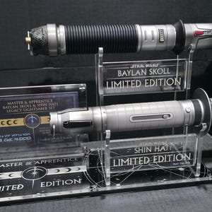May include: Two lightsabers on display, one black and silver, the other silver. The display includes text that reads "BAYLAN SKOLL LIMITED EDITION" and "SHIN HATI LIMITED EDITION". A third display reads "MASTER & APPRENTICE LEGACY LIGHTSABER SET".