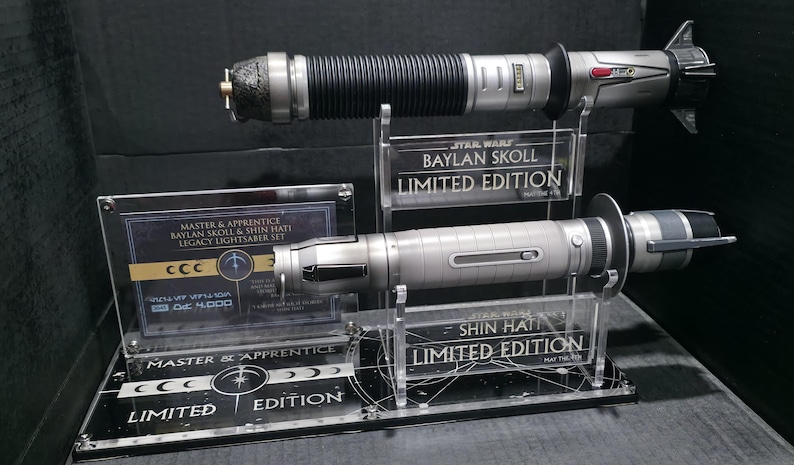 May include: Two lightsabers on display, one black and silver, the other silver. The display includes text that reads "BAYLAN SKOLL LIMITED EDITION" and "SHIN HATI LIMITED EDITION". A third display reads "MASTER & APPRENTICE LEGACY LIGHTSABER SET".