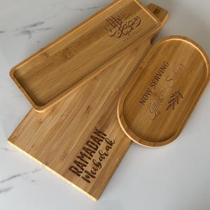 May include: Three wooden serving trays with engraved text. The largest tray says "Ramadan Mubarak". The medium tray says "Now Serving Iftar & Suhoor". The smallest tray has Arabic calligraphy.