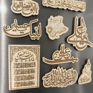Könnte beinhalten: Eine Sammlung von Holzmagneten mit arabischer Kalligraphie. Die Magnete haben verschiedene Formen und Größen mit aufwendigen Textdesigns in Hellbraun. Die Magnete werden auf einer silbernen Oberfläche präsentiert.