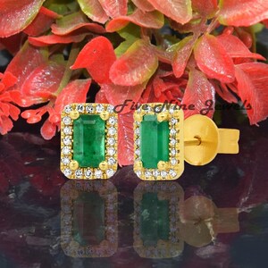 May include: A pair of gold earrings featuring emerald green gemstones surrounded by a halo of smaller diamonds. The earrings are set against a white background.