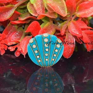 May include: A turquoise blue and gold round button with a decorative design of white dots and gold lines. The button has a raised centre and a flat back.