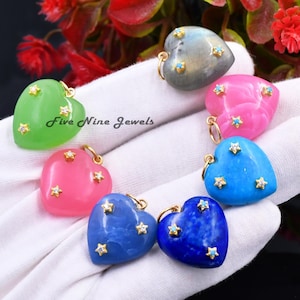 Puede incluir: Una colección de colgantes en forma de corazón en varios colores, incluyendo verde, rosa, azul y gris. Cada colgante está adornado con detalles dorados y pequeñas decoraciones en forma de estrella. El texto "Five Nine Jewels" es visible.