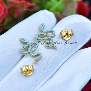 May include: A pair of gold snake earrings with turquoise stones. The earrings are on a white surface. Five Nine Jewels is written on the surface.