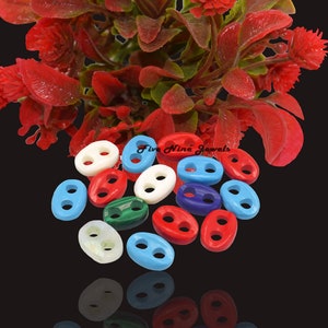 Könnte beinhalten: Sortiment an bunten ovalen Knöpfen mit zwei Löchern. Die Knöpfe sind aus verschiedenen Materialien gefertigt, darunter Rot, Blau, Weiß, Grün und Schwarz. Die Knöpfe sind auf einem schwarzen Hintergrund in einem Stapel angeordnet.