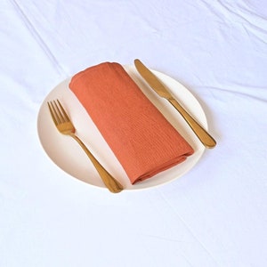 Puede incluir: Un plato blanco con una servilleta de lino naranja doblada, un tenedor dorado y un cuchillo dorado.