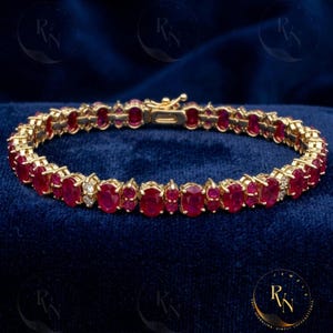 May include: A gold bracelet featuring oval-cut red gemstones and small accent diamonds. The bracelet is set in a gold metal and has a secure clasp. The gemstones are evenly spaced along the bracelet's length.