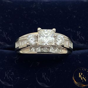 May include: A platinum engagement ring with a large square-cut center stone, flanked by two round diamonds and smaller stones along the band. The ring is set against a dark blue background.