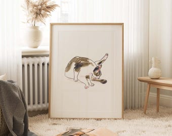 Op de afbeelding: Een ingelijste illustratie van een bruine, witte en zwarte kat die zichzelf verzorgt. De kat ligt op zijn zij en heeft zijn hoofd naar de zijkant gedraaid. De illustratie is op een witte achtergrond en is ingelijst in een licht houten lijst.