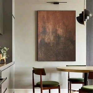 May include: Abstract painting with brown, orange, and gold hues. The painting has a textured, layered look, with darker shades in the bottom half and lighter shades in the top half. The painting is hanging on a wall in a modern dining room.
