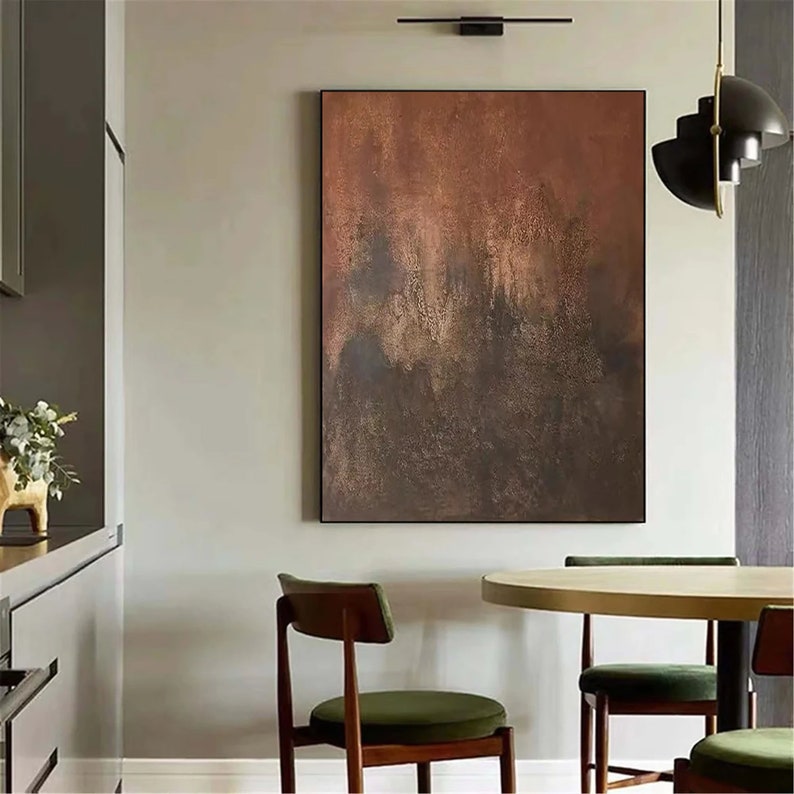 May include: Abstract painting with brown, orange, and gold hues. The painting has a textured, layered look, with darker shades in the bottom half and lighter shades in the top half. The painting is hanging on a wall in a modern dining room.