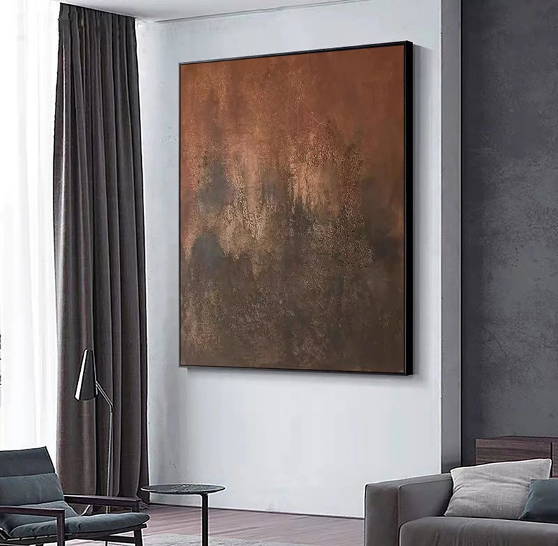 May include: Abstract painting with brown, orange, and grey hues. The painting has a textured, layered look, with areas of darker and lighter shades. It is framed in a black frame.