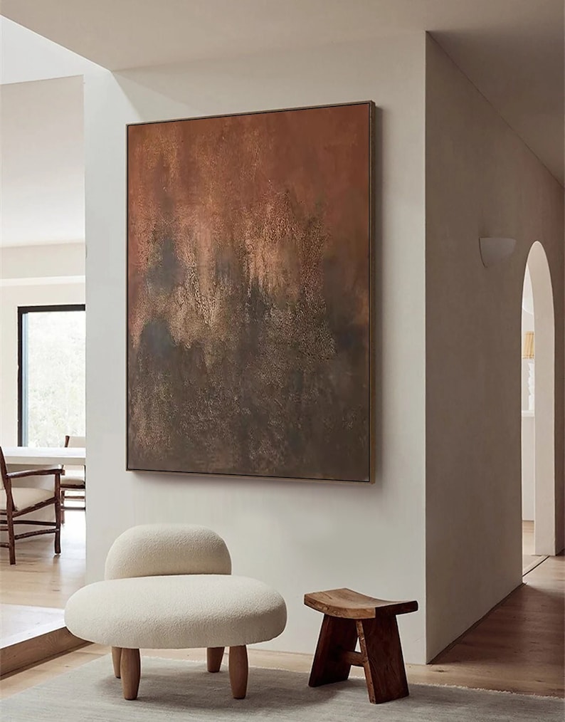May include: A white, fluffy, round chair with wooden legs sits next to a wooden stool in a modern living room. A large abstract painting with brown, orange, and blue hues hangs on the wall behind the chair.