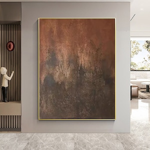 May include: Abstract painting with brown, orange, and gold hues. The painting has a textured, layered look, with areas of darker brown and lighter gold. The painting is framed in a thin gold frame.