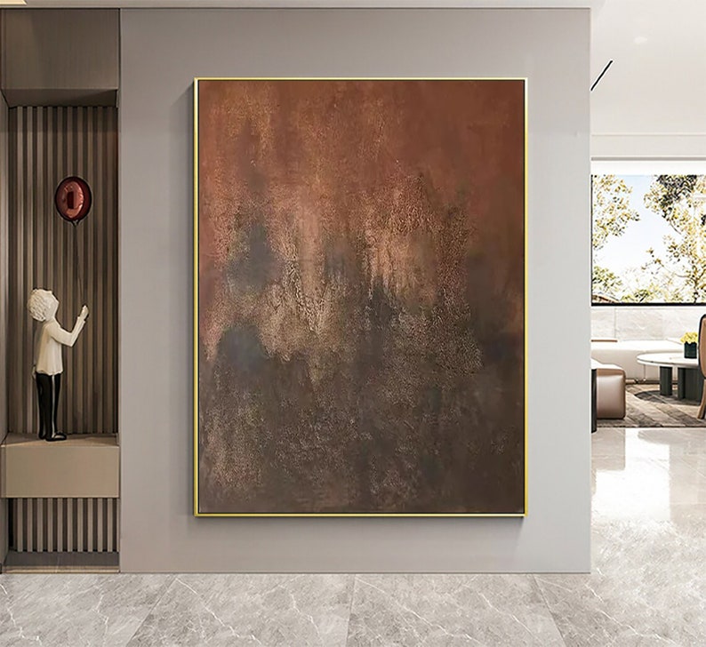 May include: Abstract painting with brown, orange, and gold hues. The painting has a textured, layered look, with areas of darker brown and lighter gold. The painting is framed in a thin gold frame.