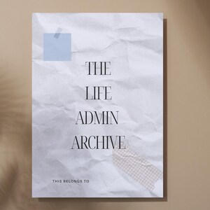 Könnte beinhalten: Ein weißes, zerknittertes Papier mit dem Text "THE LIFE ADMIN ARCHIVE" in einer Serifenschrift, befestigt mit blauem Klebeband und gemustertem Washi-Tape. Die Worte "THIS BELONGS TO" stehen unten. Der Hintergrund ist ein neutrales Beige mit Schatten.