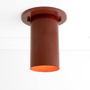 May include: A red cylindrical ceiling light fitting with a round base. The light is on and emits a warm orange glow.