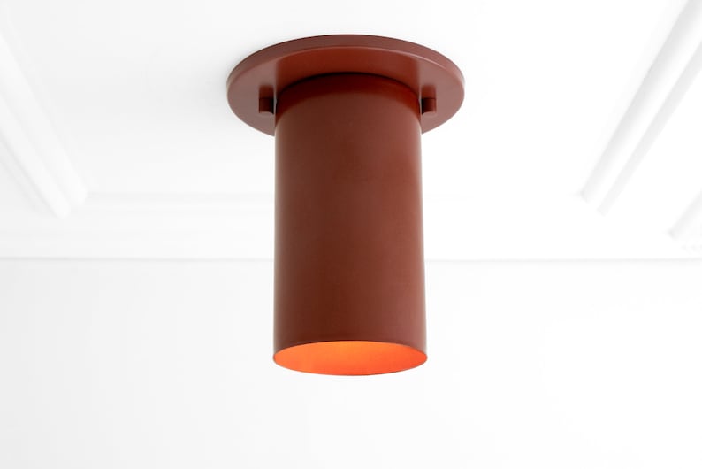 May include: A red cylindrical ceiling light fitting with a round base. The light is on and emits a warm orange glow.