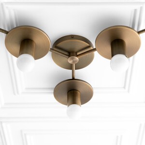 May include: A brass ceiling light fixture with three arms and three round shades. Each arm has a light bulb and a small, round, decorative piece at the end.