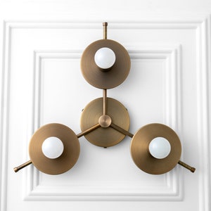 May include: A brass wall sconce with three circular light fixtures. Each fixture has a white globe light bulb.