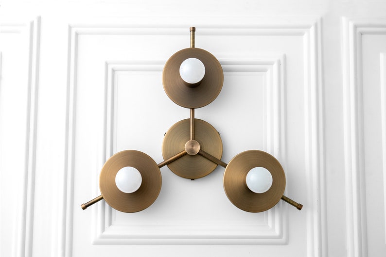 May include: A brass wall sconce with three circular light fixtures. Each fixture has a white globe light bulb.