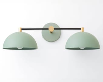 May include: A wall-mounted light fixture with two green dome-shaped shades and a black metal arm. The fixture has a gold finish.