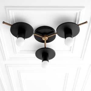 May include: A three-light ceiling fixture with black metal shades and gold accents. The fixture has a modern design and is perfect for a contemporary home.