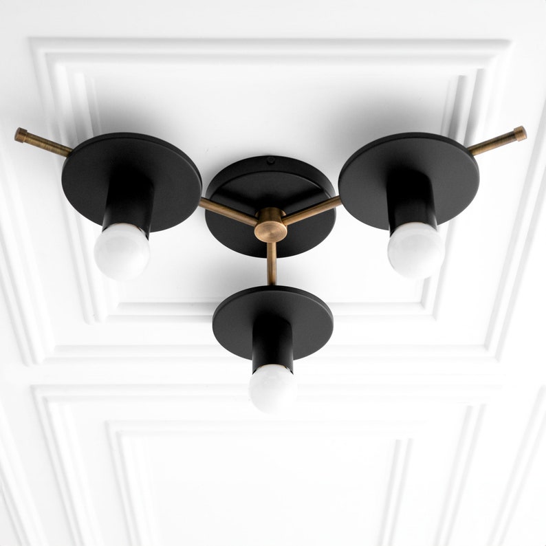 May include: A three-light ceiling fixture with black metal shades and gold accents. The fixture has a modern design and is perfect for a contemporary home.