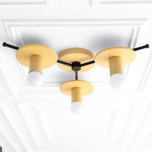 May include: A three-light ceiling fixture with yellow metal shades and black metal arms. The fixture has a modern design and is suitable for a variety of interior styles.
